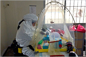 Man in hazardous-material suit manipulating material inside plastic enclosure (DOD/U.S. Navy Chief Petty Officer Jerrold Diederich)